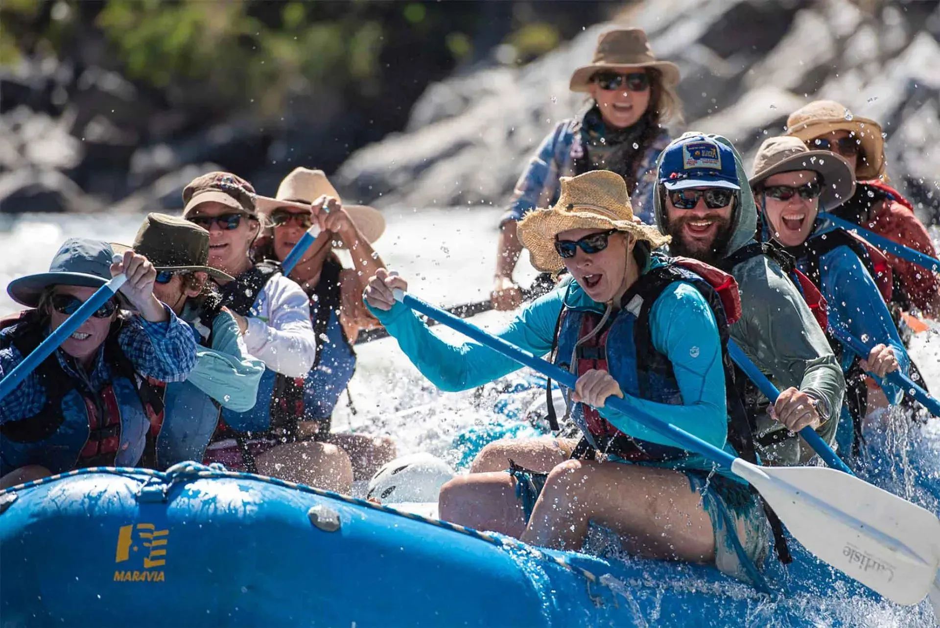 Group rafting on whitewater, paddlers in blue rafts splashing through rapids with helmets and life jackets