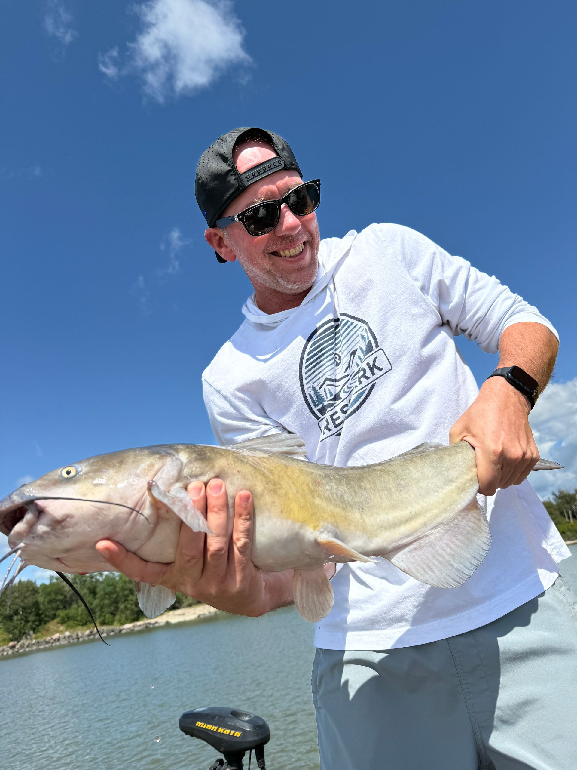 Man holding a large fish on a boat under a clear blue sky