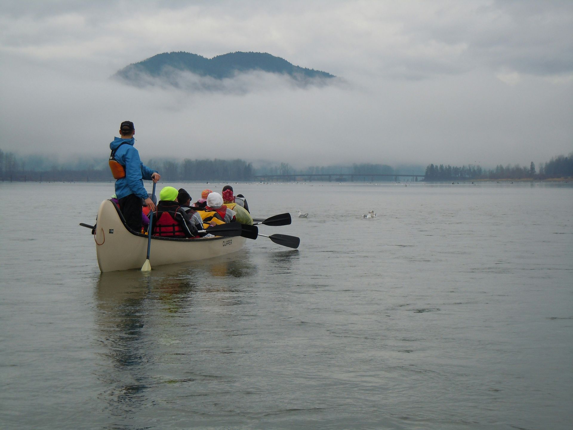 People in a small boat on a calm lake, with misty mountains in the background