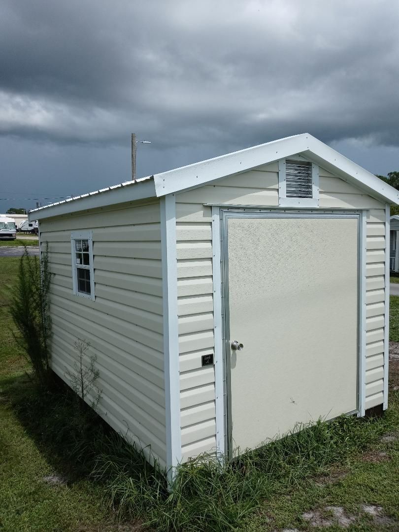 A small white shed with a window is sitting in the grass.
