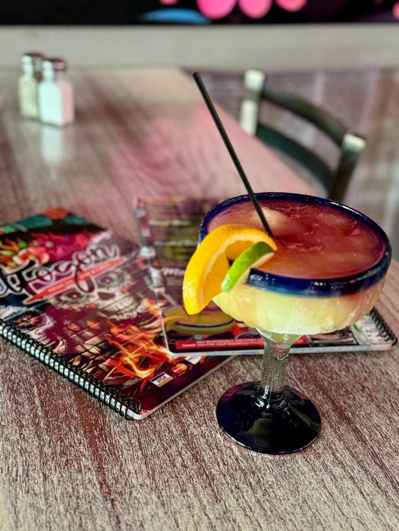 Frozen margarita with orange and lime garnish on a table next to a restaurant menu.