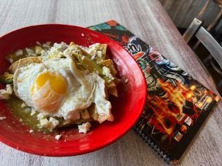 Chilaquiles with fried egg on red plate, beside patterned napkin.