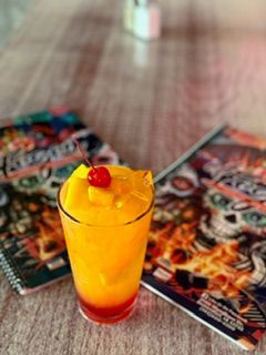 Orange layered tropical drink with a cherry on top, next to two colorful menus.
