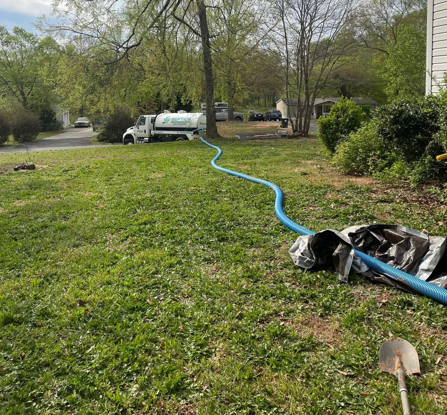 A septic truck with a blue hose on a grassy lawn.