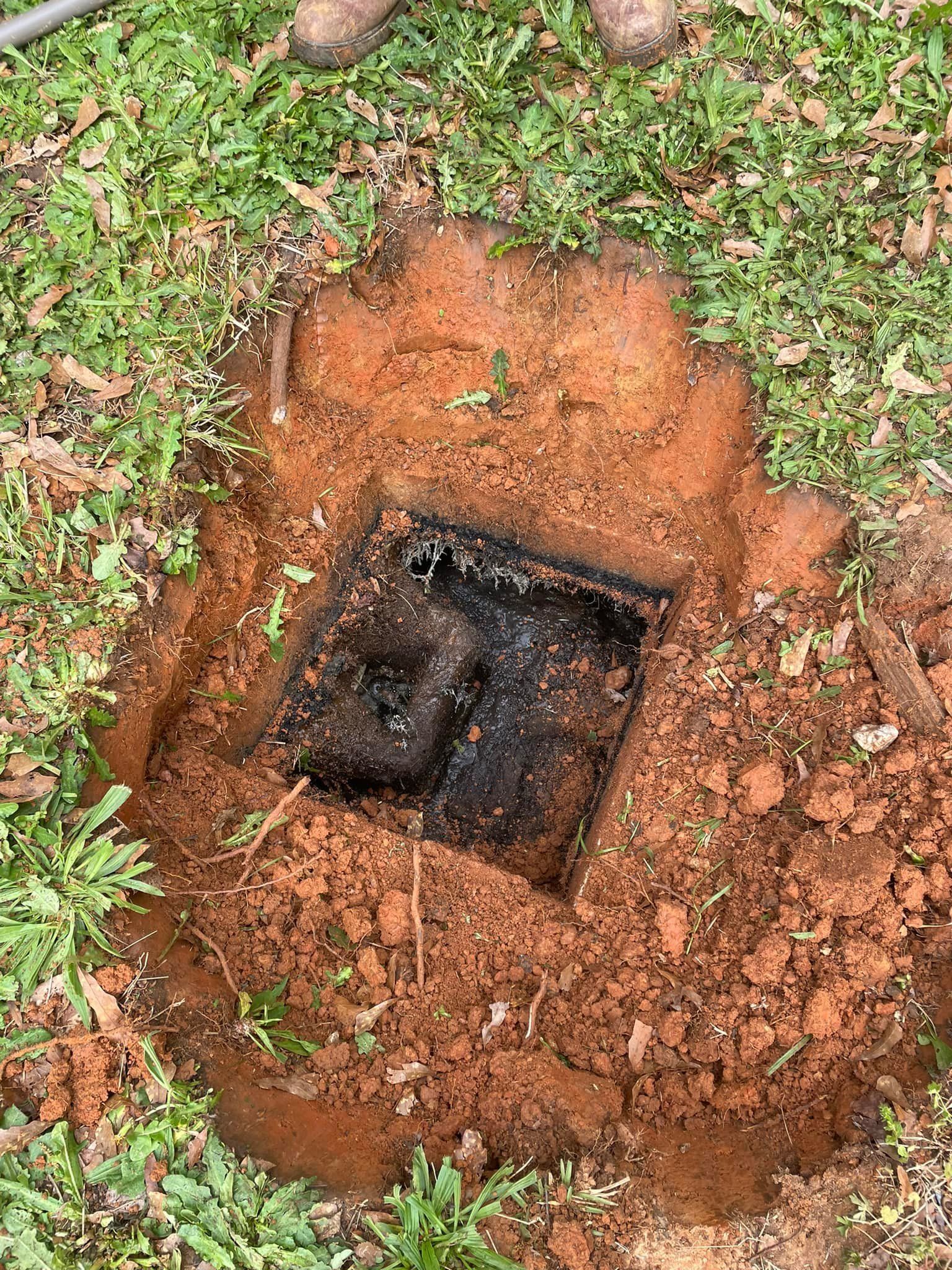 Excavated square black septic tank access in dirt, surrounded by grass.
