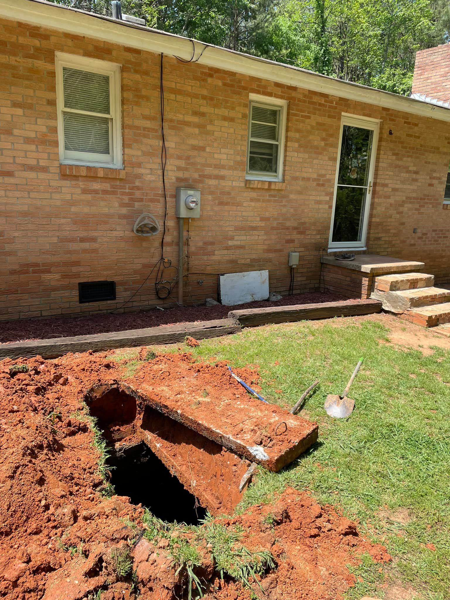 Red brick house exterior with a hole in the ground and a raised concrete cover in the foreground.