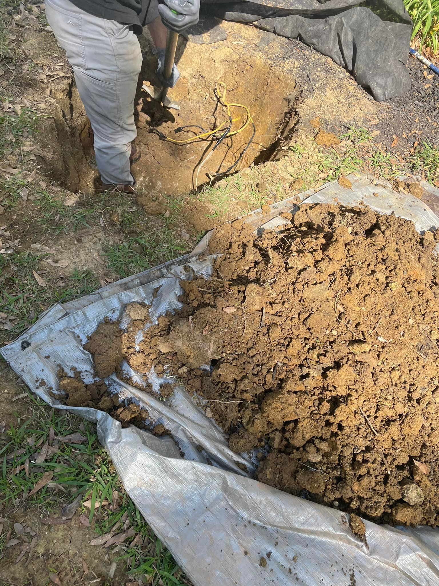 Person digging in soil, using a tool. Pile of soil on a tarp. Outdoors.