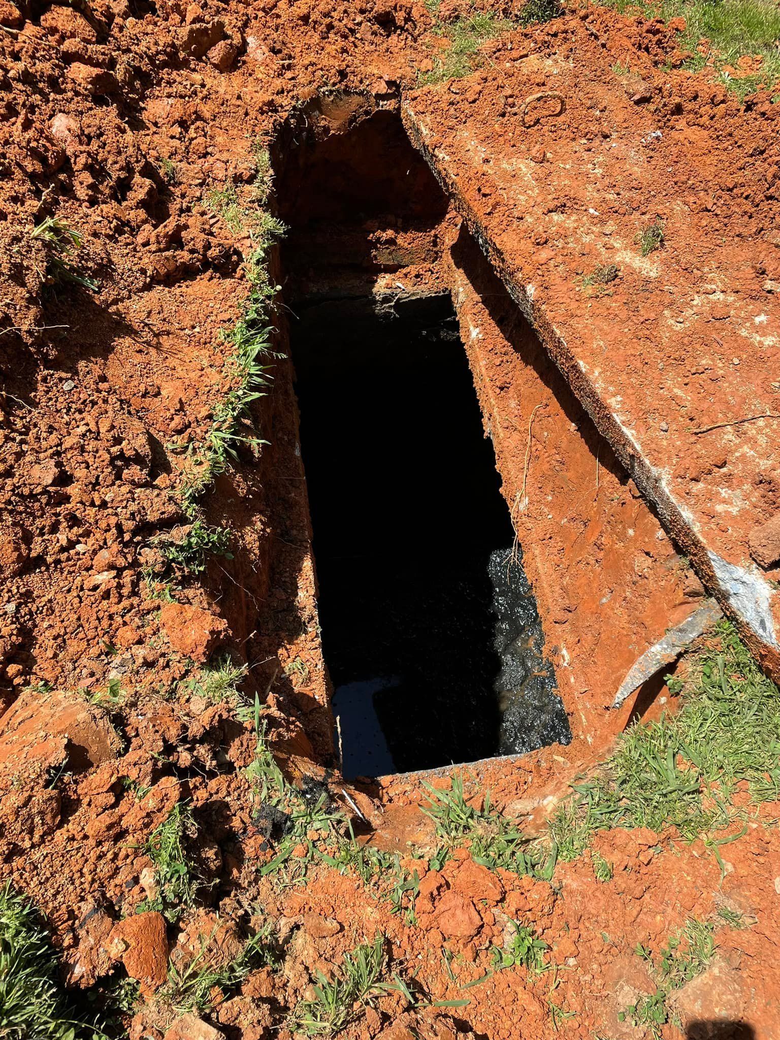Hole dug into red dirt, with dark interior, pickaxe at the edge.