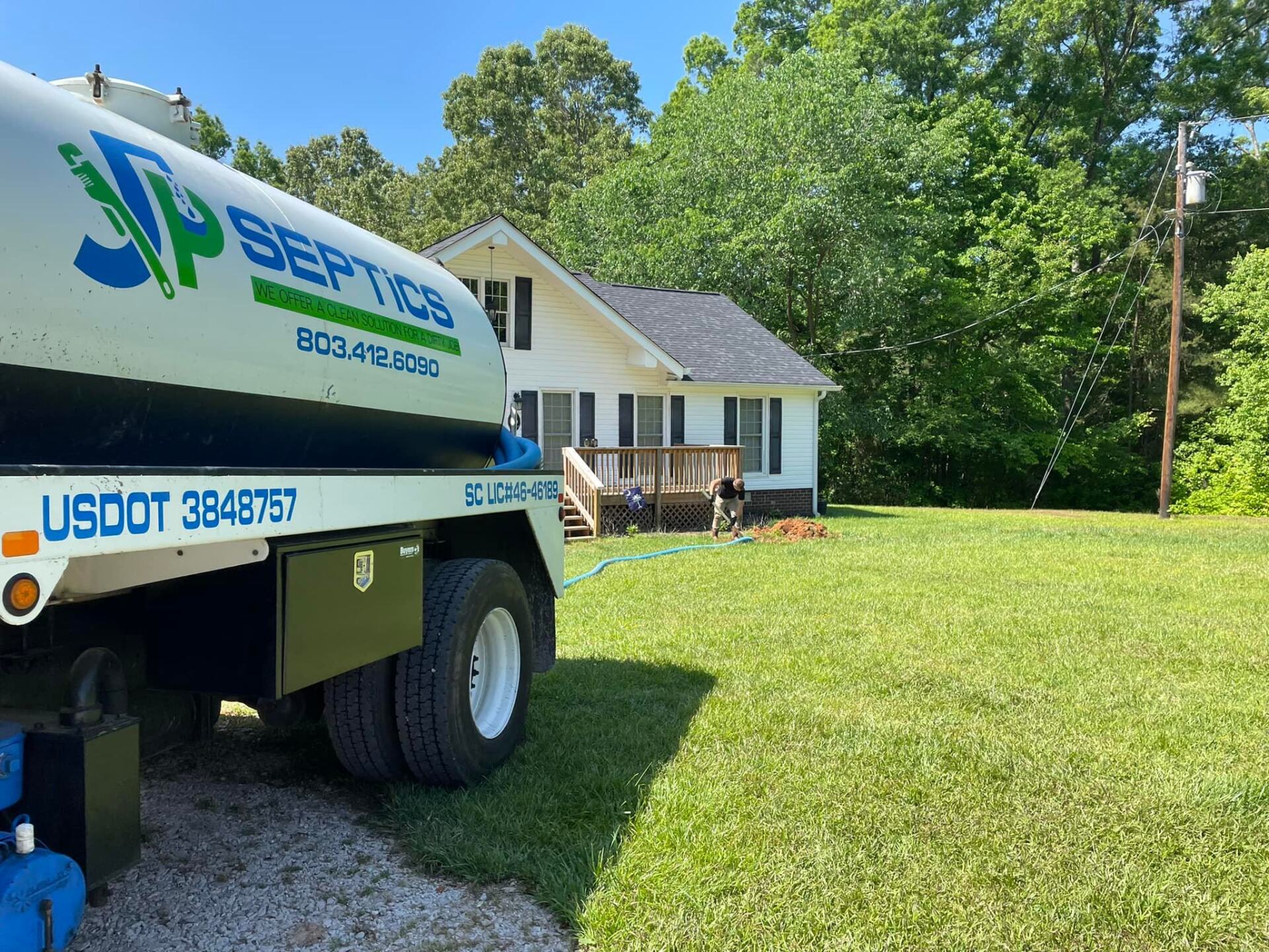 White septic truck parked near a small white house on a sunny day.