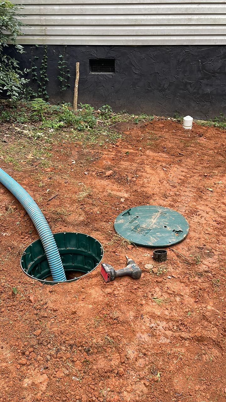 Open septic tank with a hose inside, and dirt around.