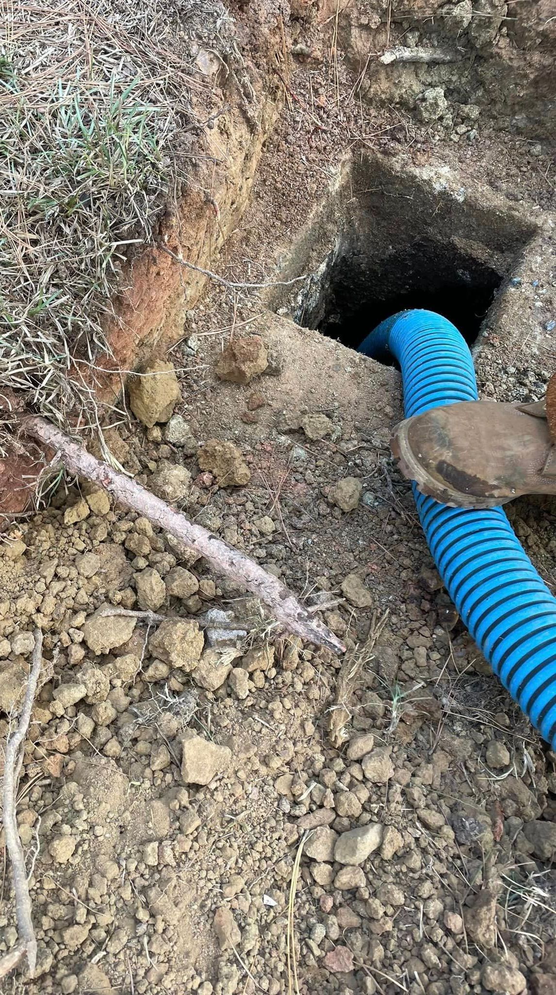 Blue corrugated pipe extends from a square hole in the dirt.