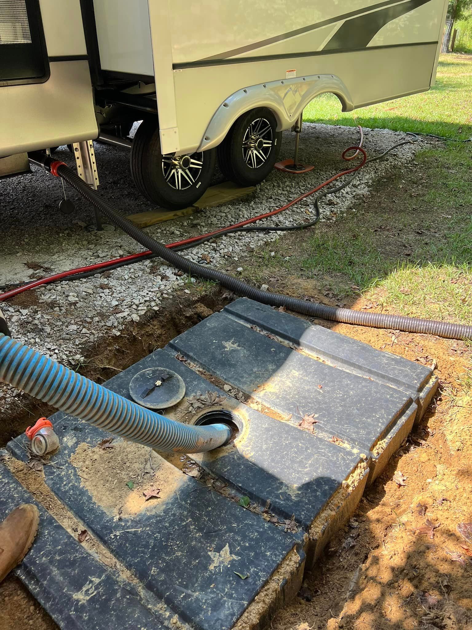 RV waste tank being emptied into a dark rectangular waste system. The process takes place outdoors.