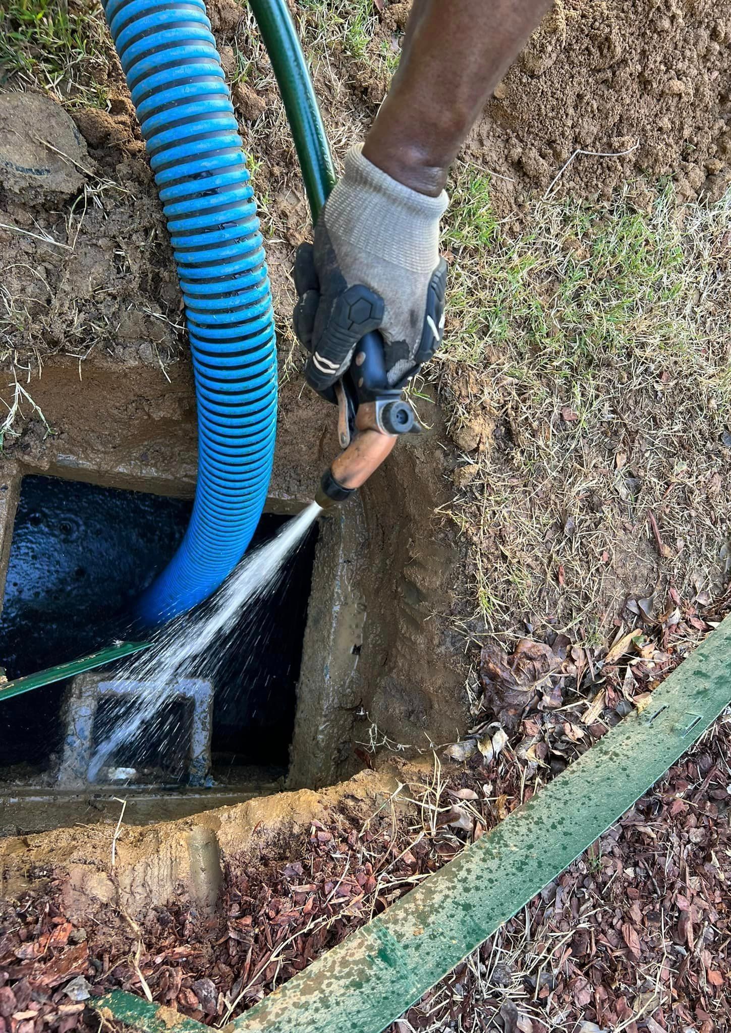 Person using hoses to clean a concrete septic tank. Water sprays out near dirt and grass.