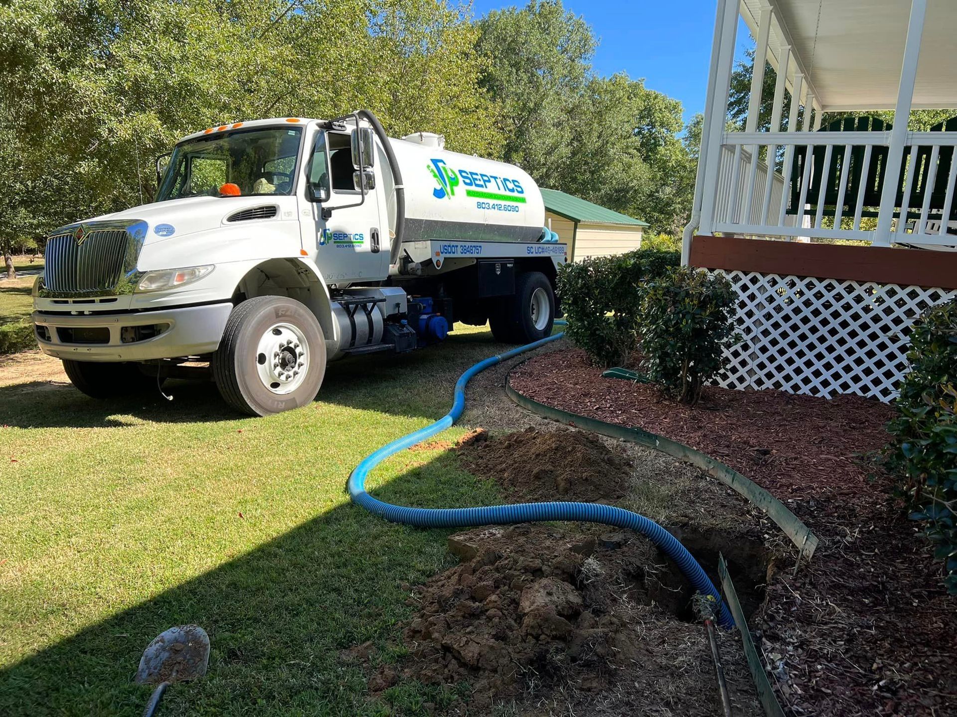 White septic service truck with blue hose connected, parked near a house, on a sunny day.