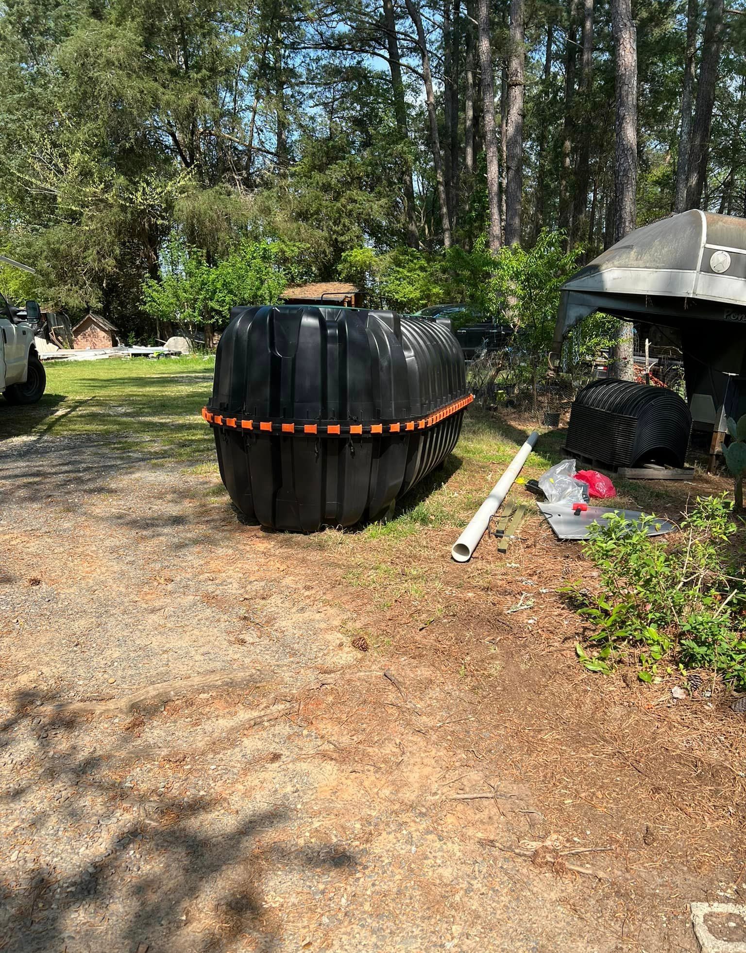 Black septic tank on gravel, with a white pipe and trees in the background.