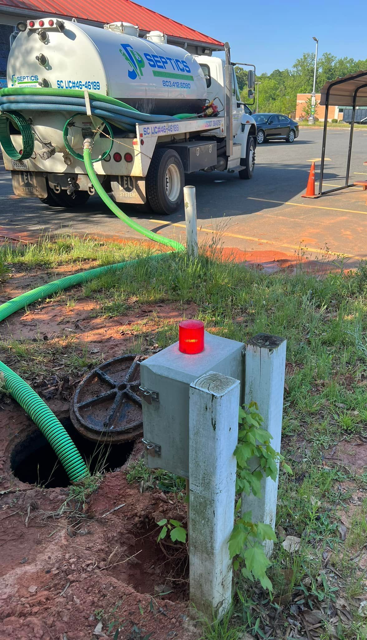 Septic service truck with hose connected to a sewer access point, red light on top of the access point.