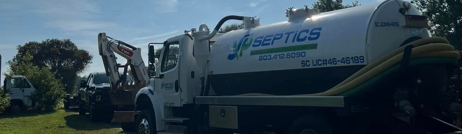 Septic tank truck and heavy equipment in front of a green field under a clear blue sky.