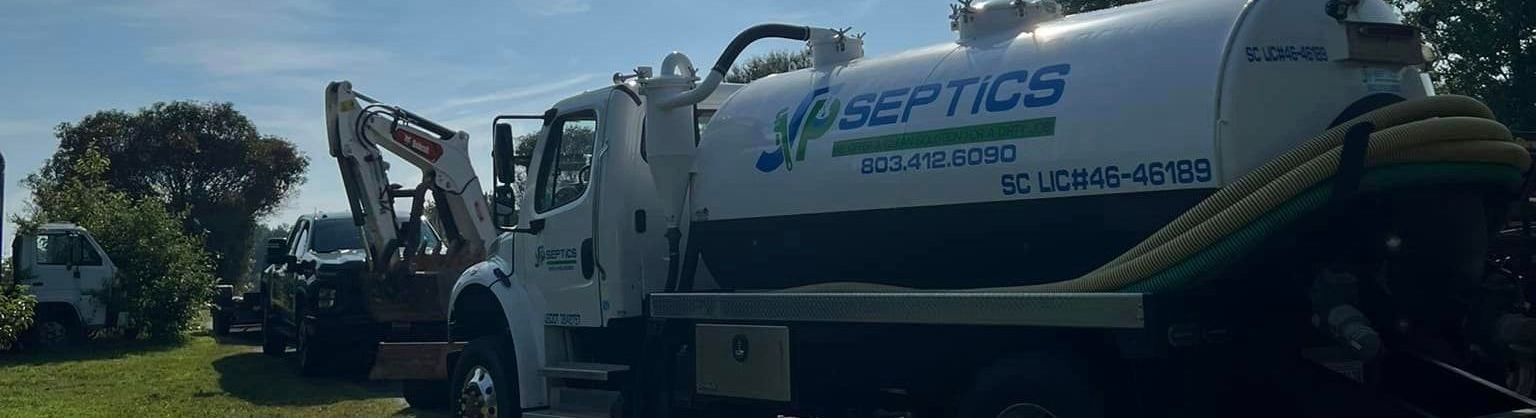Septic tank truck parked outside near other machinery and foliage.