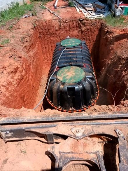 Black septic tank in a red clay pit, with two green access covers.