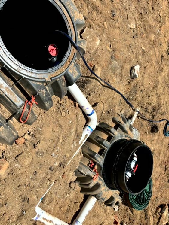 Two black septic tanks with open lids and connected pipes sit in dirt.