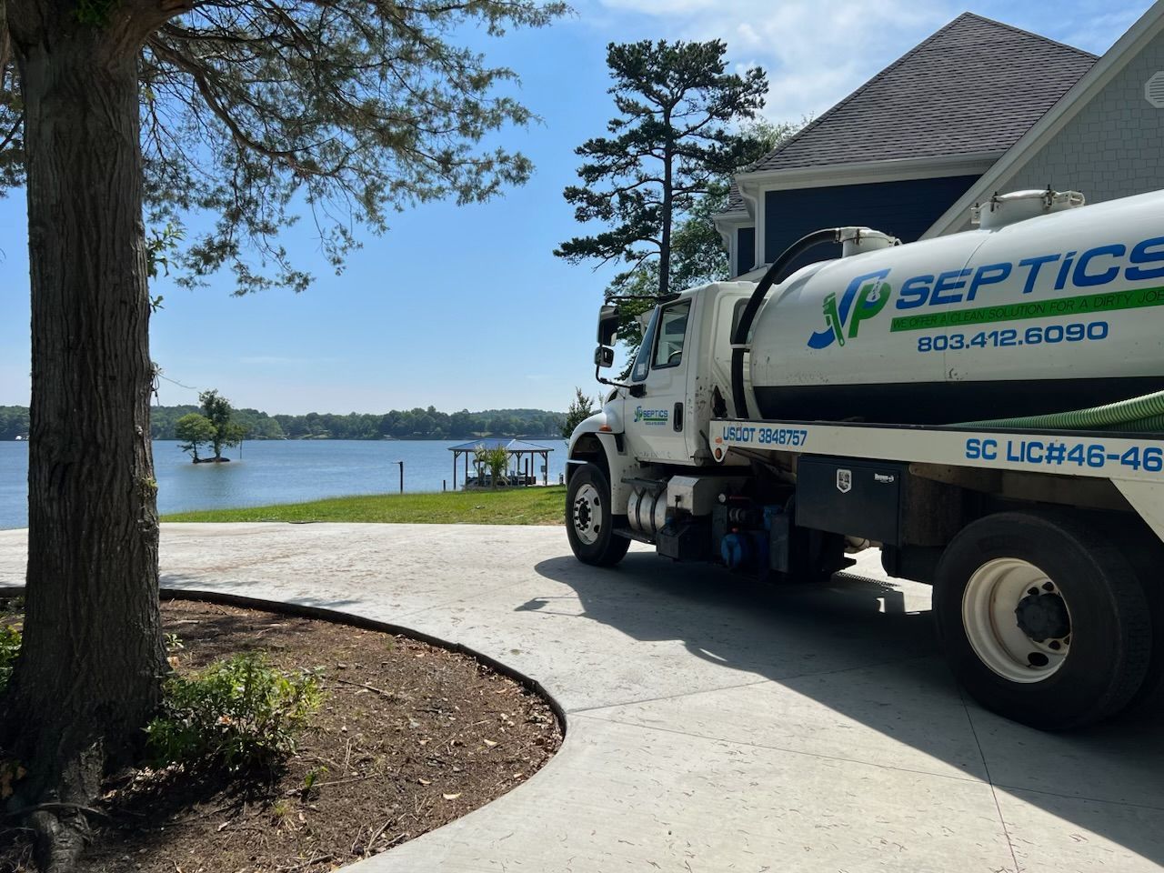 Septic tank truck parked on a driveway near a lake, sunny day.
