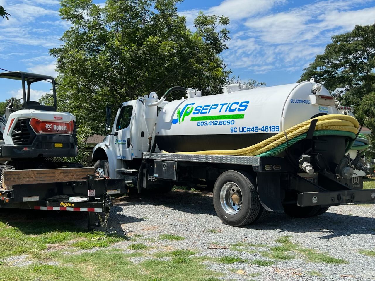 Septic service truck with a Bobcat excavator on a trailer in a residential setting.
