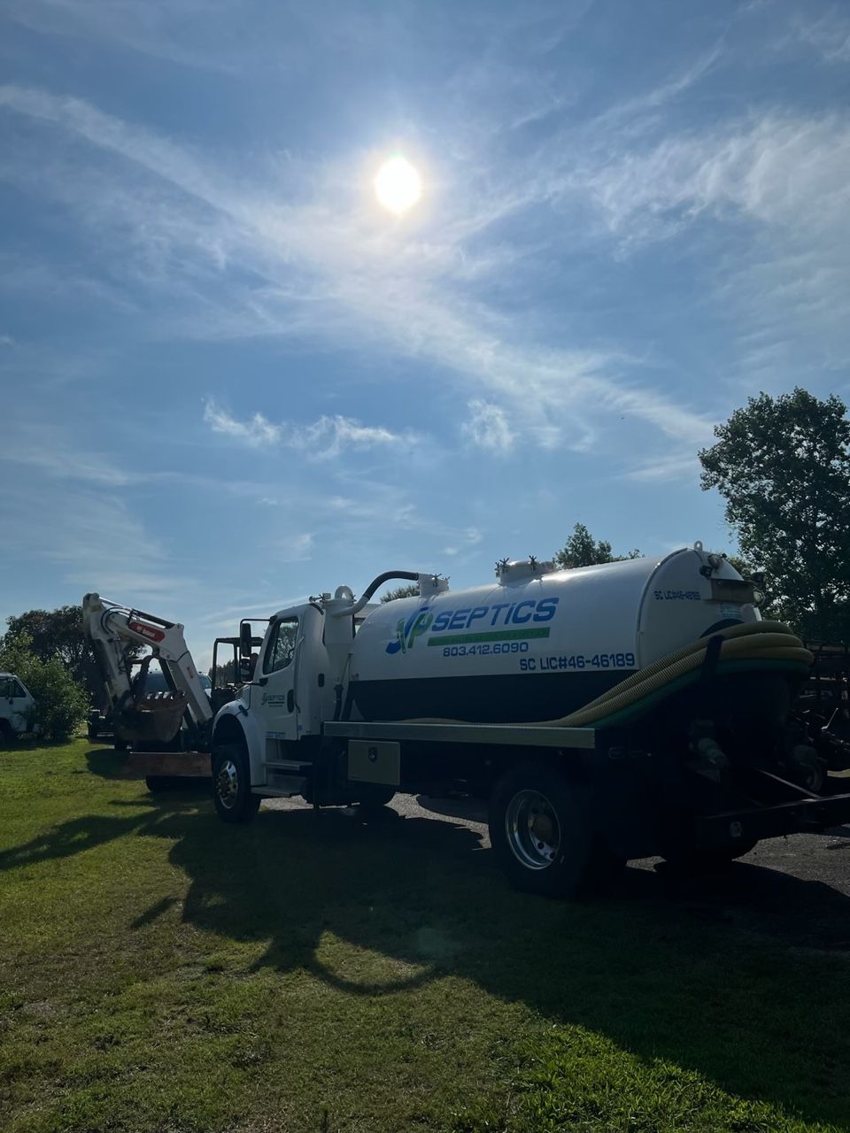 Septic service truck on a grassy lawn under a sunny sky.