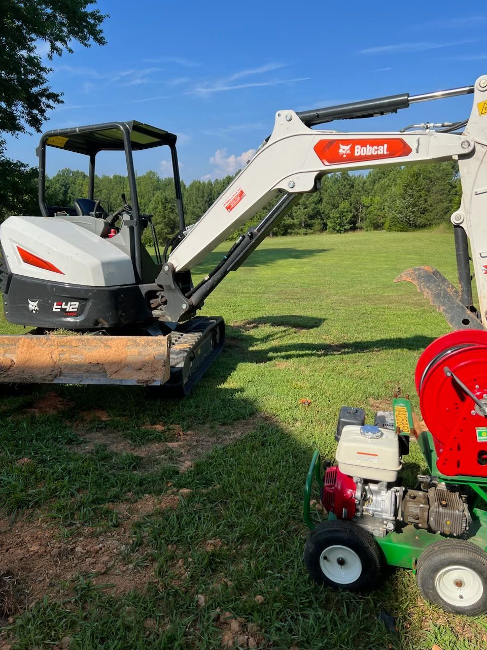 Bobcat excavator and trencher on grass under a blue sky, ready for digging.