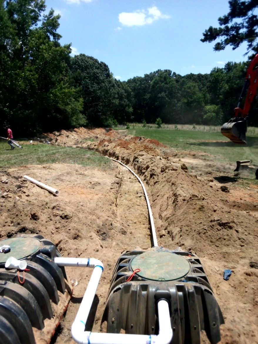 Septic system installation: Excavation, tanks, and pipes in a grassy field on a sunny day.