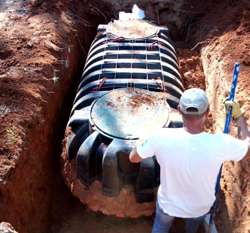 Man installing a black septic tank in a dirt trench, using a level.