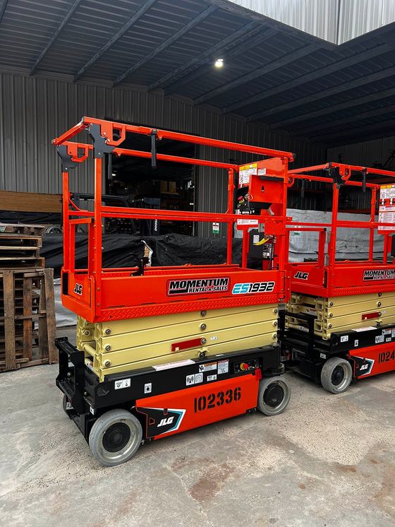 Two orange scissor lifts are parked next to each other in a warehouse.