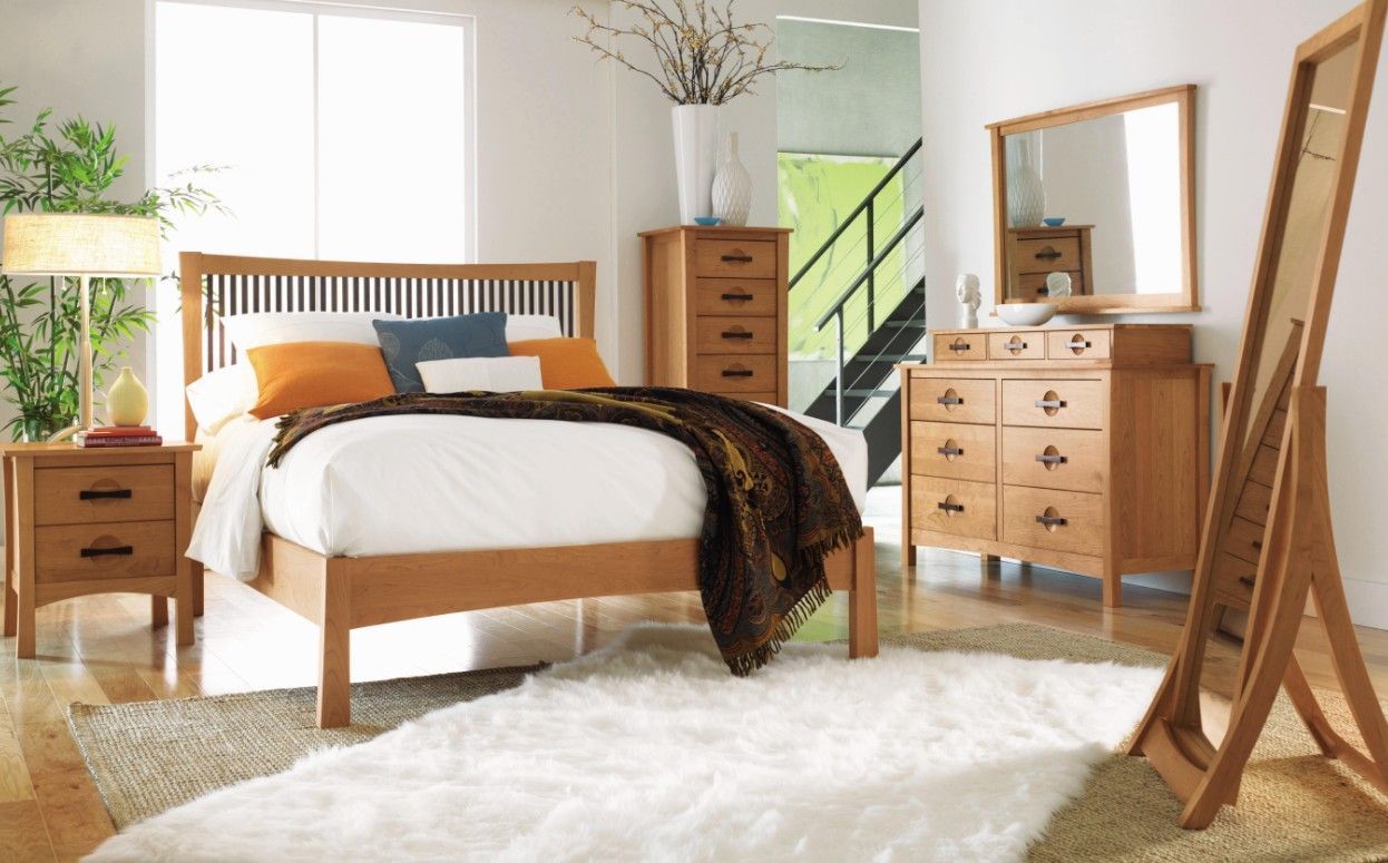 Two wooden beds with patterned quilts in a rustic bedroom setting, separated by a nightstand and lamp
