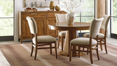 Dining room with a round wooden table, four upholstered chairs, sideboard, and large windows in warm natural light