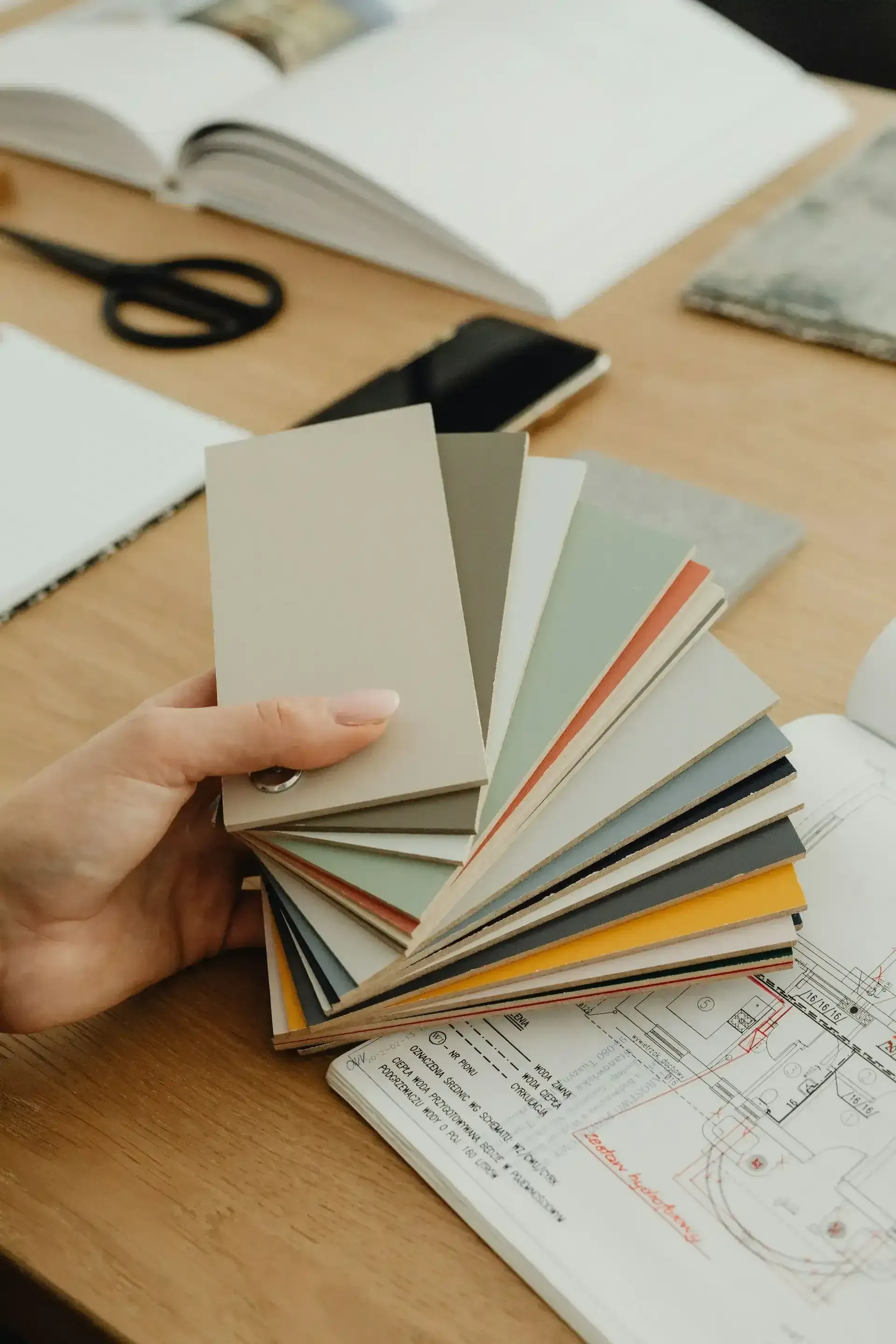 Hand holding a fan of color swatches on a wooden surface
