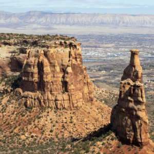 Desert canyon buttes and red rock spires under a hazy blue sky, with distant mesas in the background
