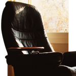 Black leather recliner by a sunlit window in a softly lit room