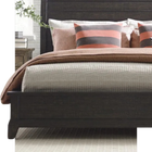 Modern bed with brown and cream bedding, striped pillows, and a plant beside it in a bright bedroom