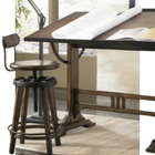 Drafting table with an open book and a stool in a bright studio workspace