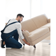 Man kneeling and lifting a beige sofa in a bright room