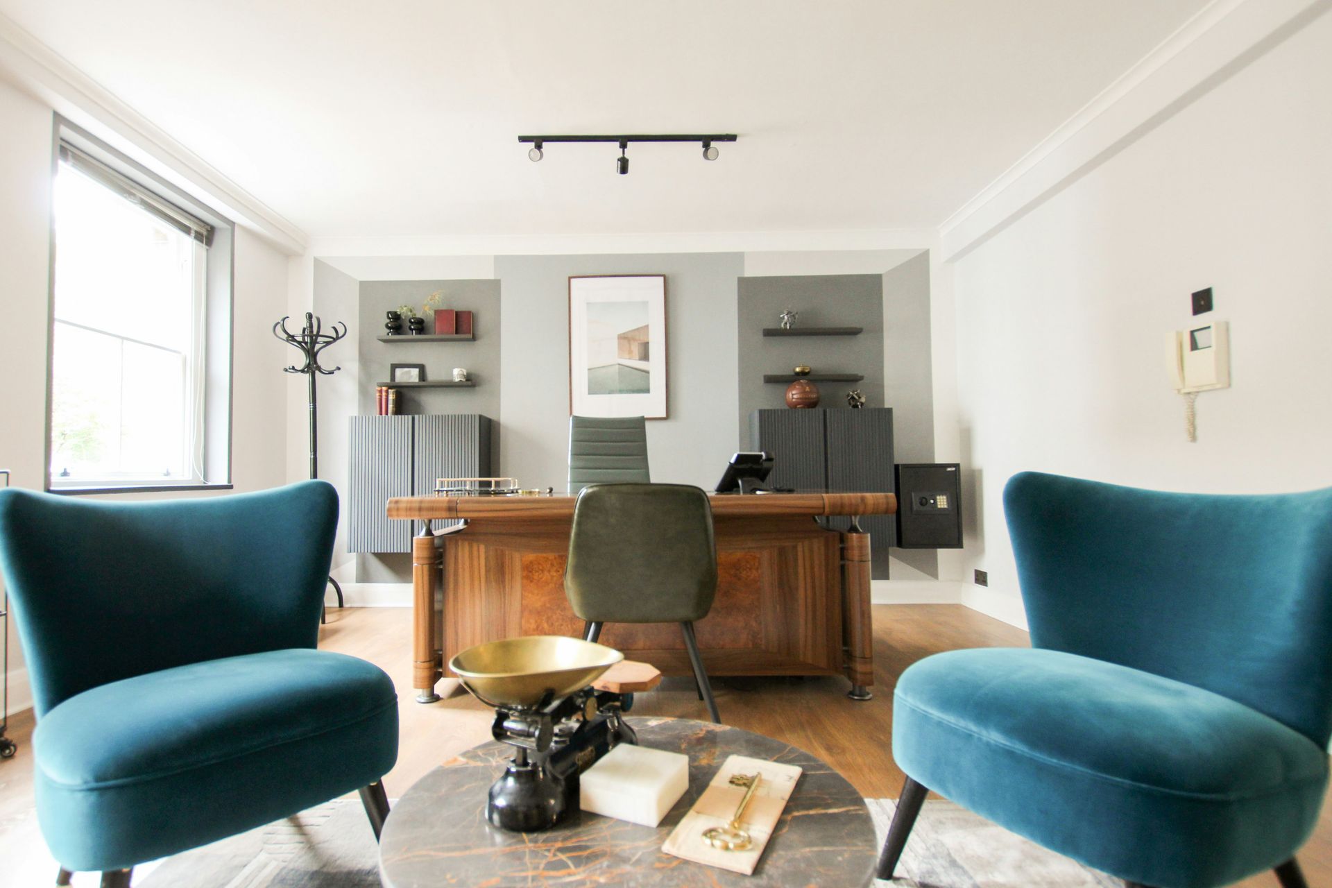 Modern living room with blue chairs, wooden desk, wall art, and a large window