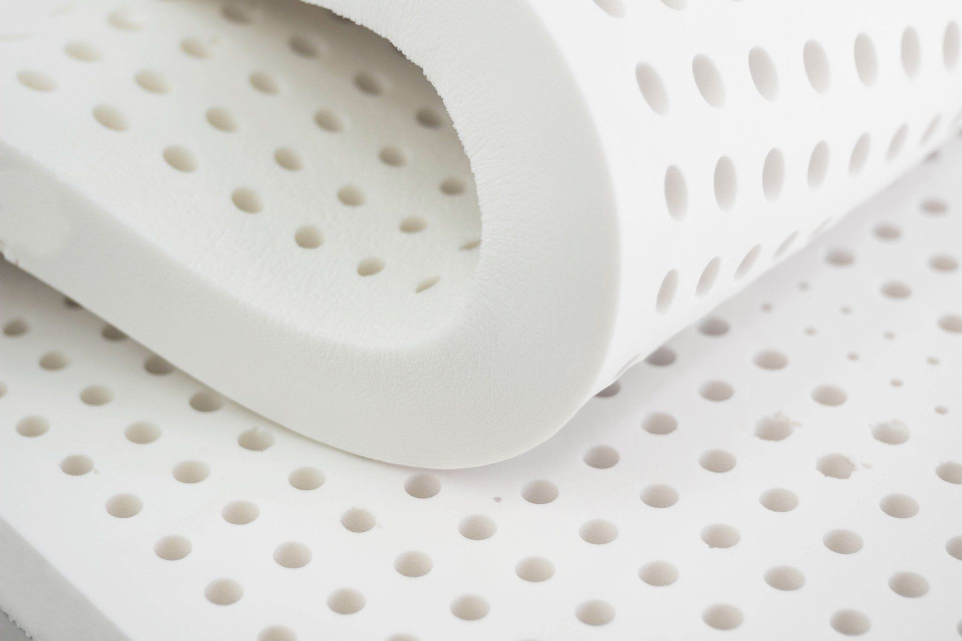Coprimaterasso in lattice bianco con fori di ventilazione, piegato per mostrare la consistenza.