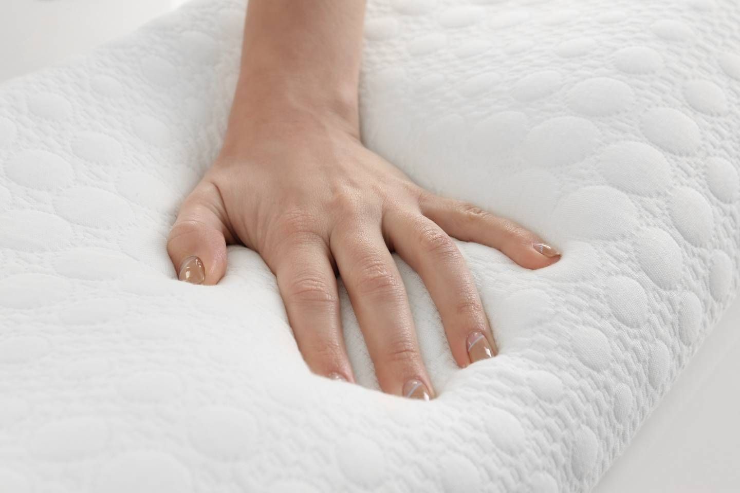 Mano che preme su un cuscino bianco e ruvido, per dimostrarne la morbidezza.