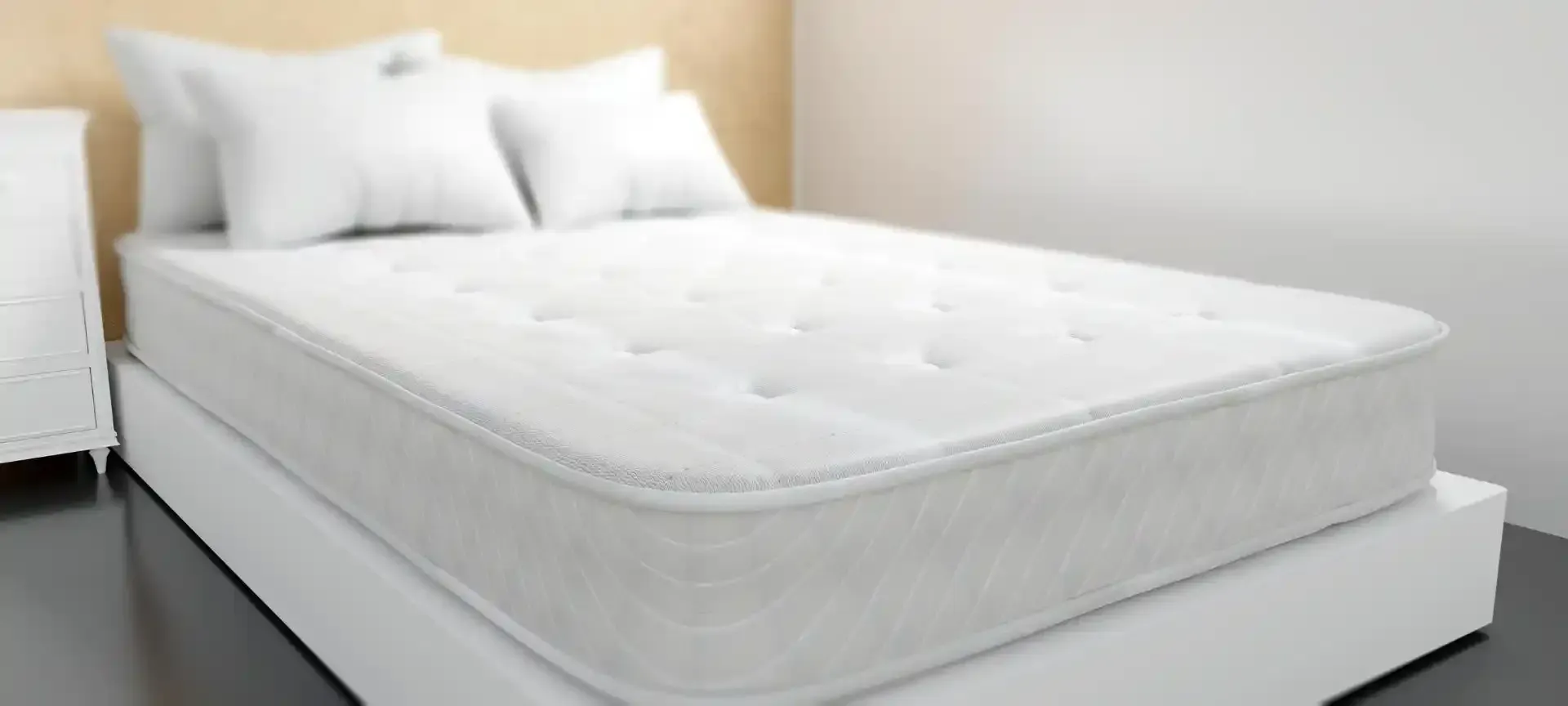 Un materasso bianco con cuscini su un letto a piattaforma bianco in una stanza dai colori chiari.