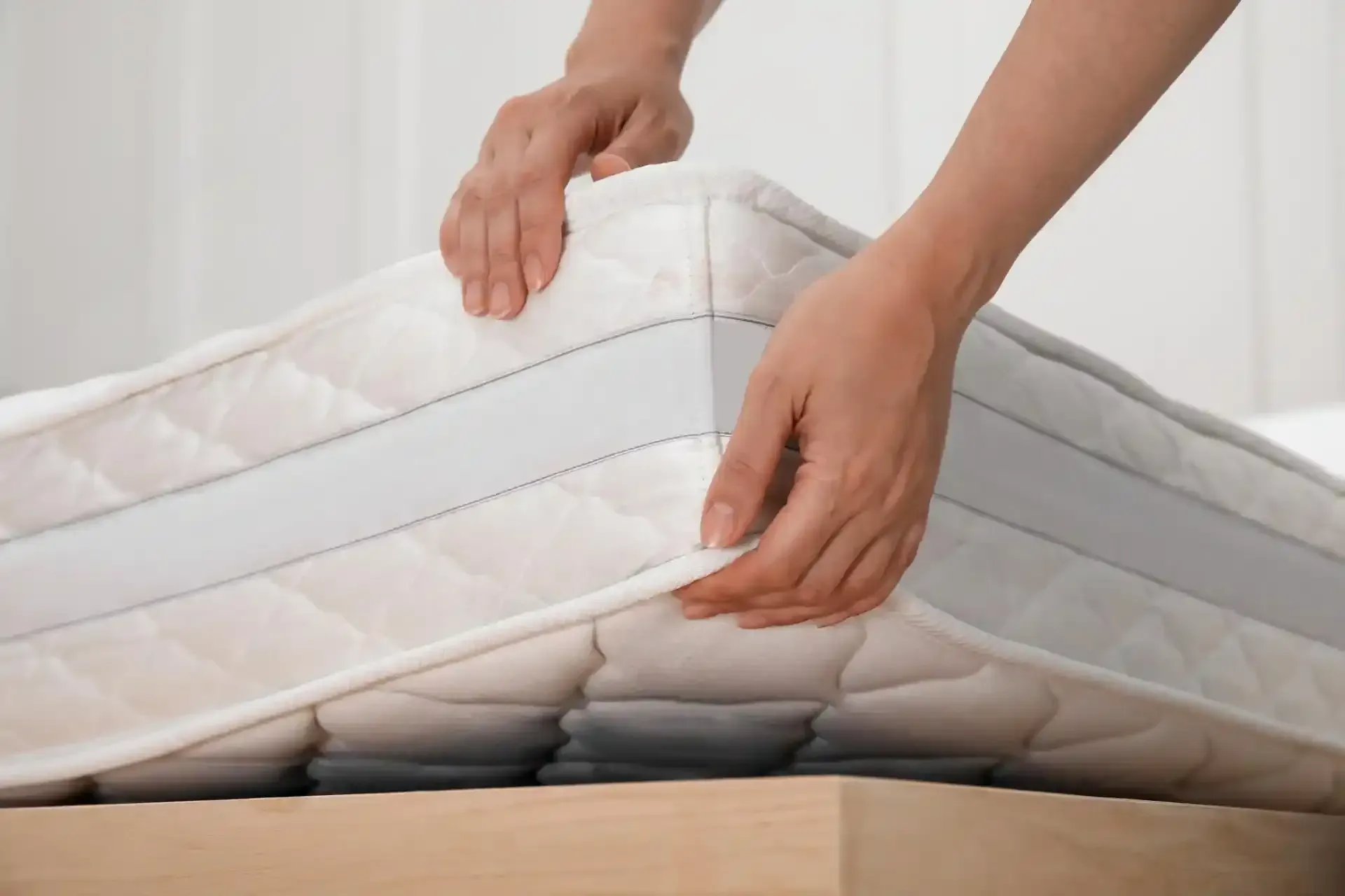 Mani che sistemano un materasso bianco su una struttura in legno del letto.
