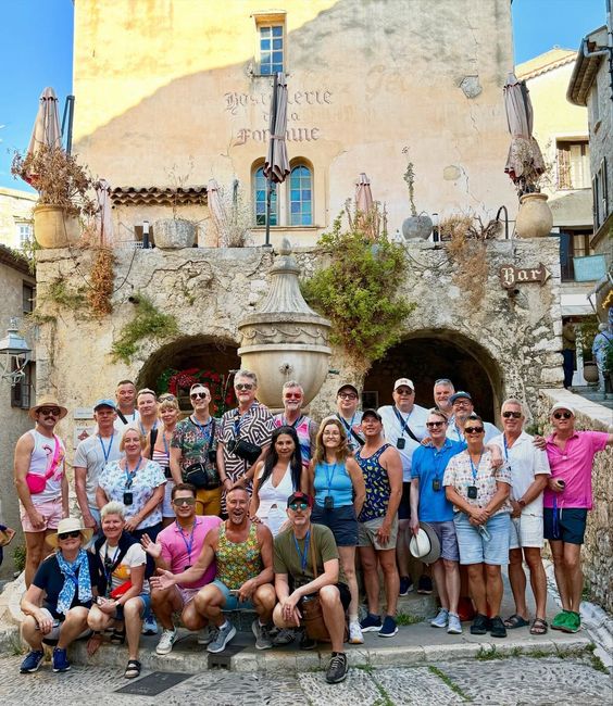 Group of tourists posing in front of a whimsical stone building with arches and a fountain