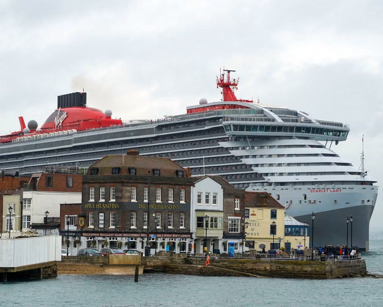 Large red-and-white cruise ship behind waterfront buildings on a cloudy day