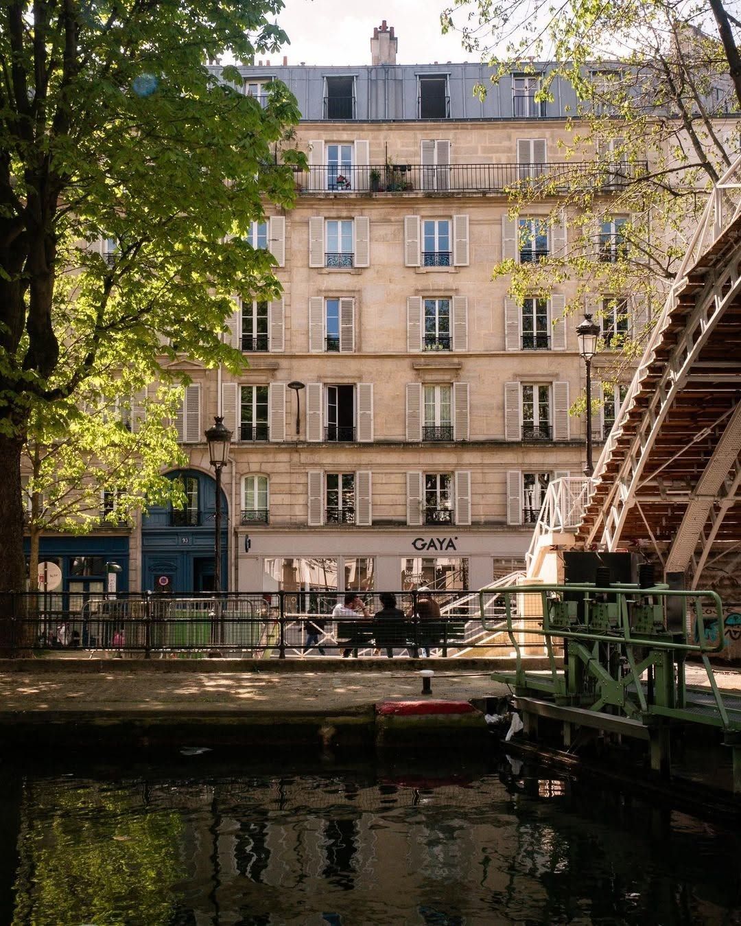 Canal scene with a cream apartment building, trees, and a bridge over calm water