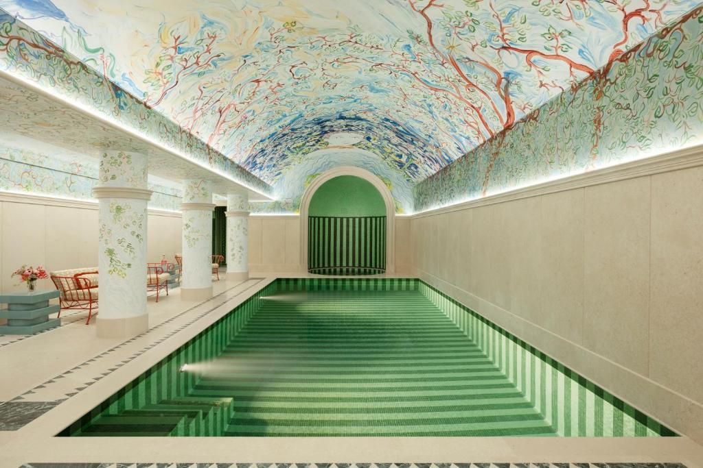 Elegant indoor pool with green steps, ornate painted ceiling, and arched doorway
