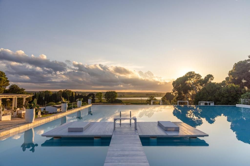Infinity pool at sunset with a wooden walkway and calm blue water under a cloudy sky