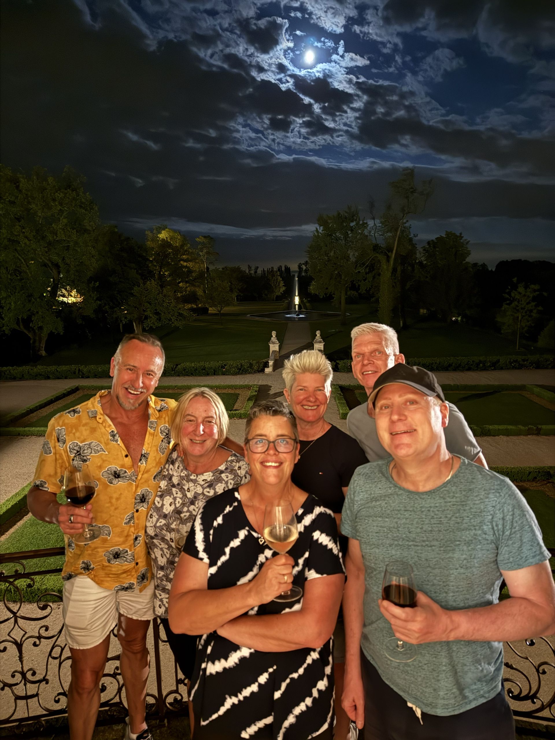 Five people smiling outdoors at night, posing in a garden under a moonlit sky.